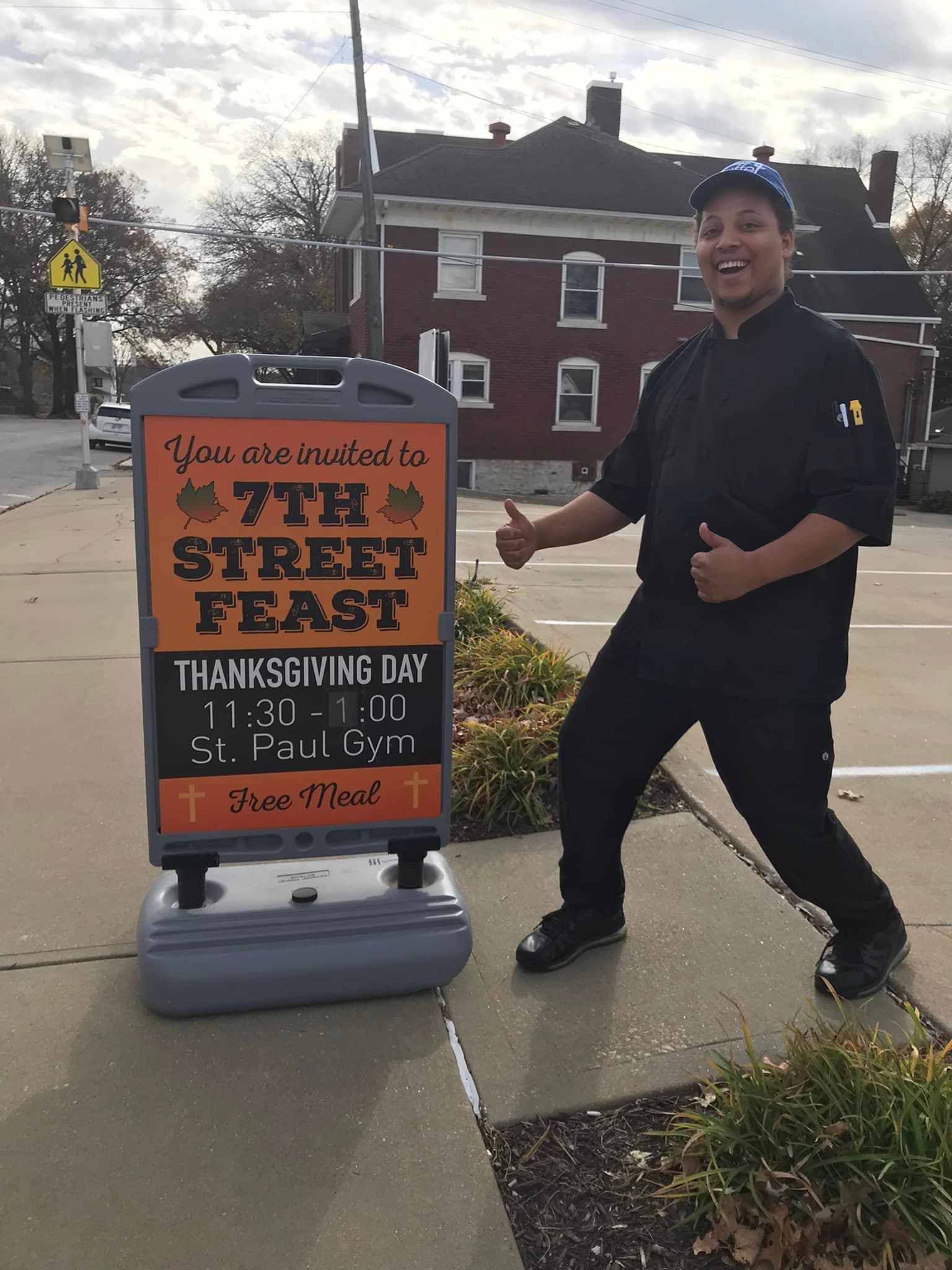Smiling man in chef's uniform gives thumbs up next to a Thanksgiving feast sign.