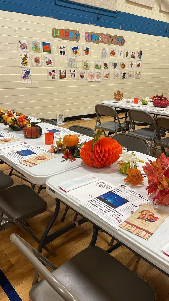 Festive community hall tables decorated with pumpkins and autumn leaves for a Thanksgiving celebration.
